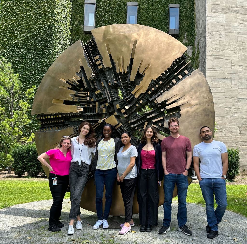 Photo of the Hayne Lab:
Cassandra, Magda, Destiny, Shreya, Ry, Daniel, Gabriel standing in front of a gold metal circle piece of art